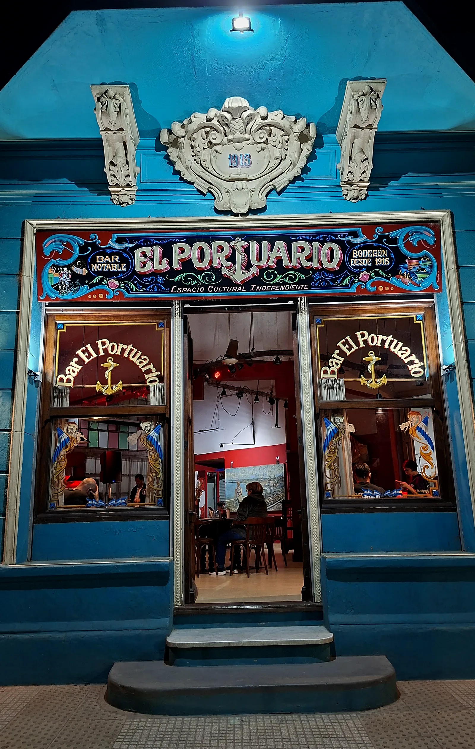 La puerta del bar abierta de noche, con el salón iluminado