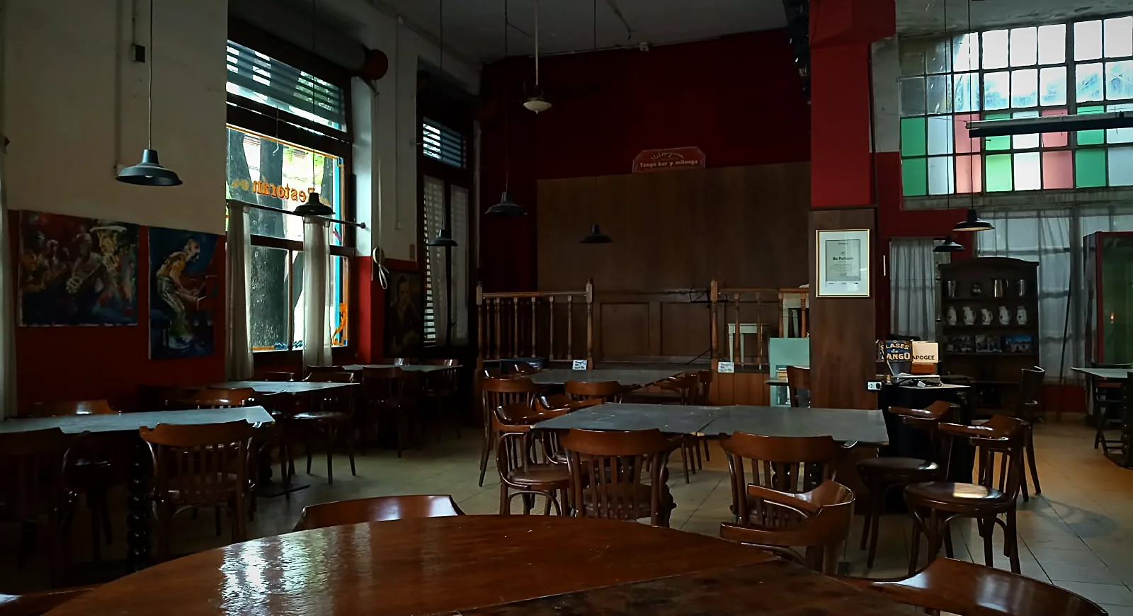 Salón del bar con mesas de madera, paredes rojas y vitrales de colores
